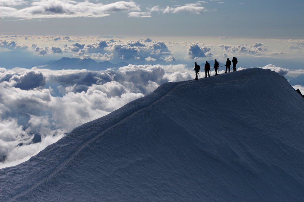 Climbers on top of snowy mountain - above the clouds